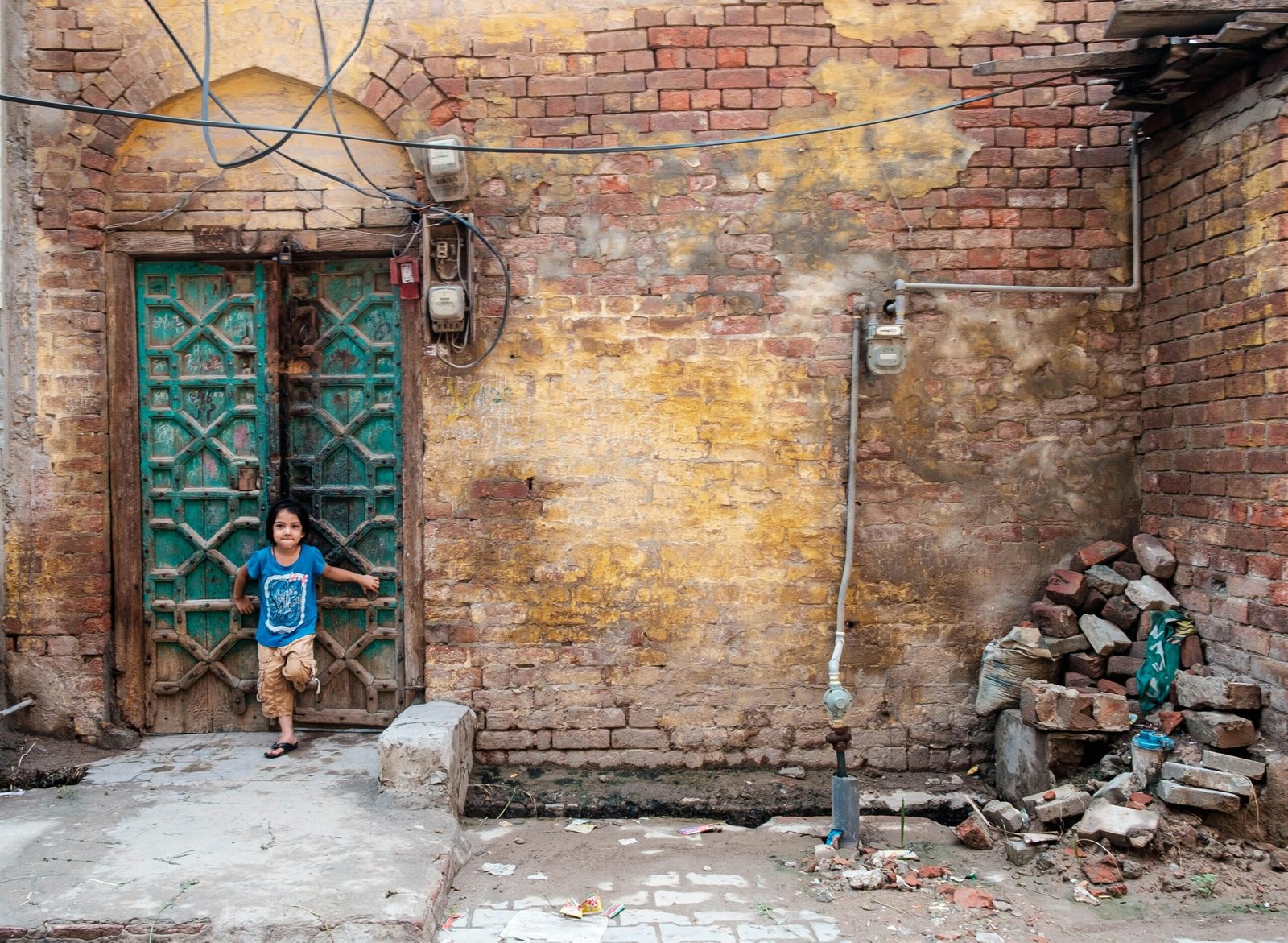 Young child in front of a vintage wooden door in Faisalabad, showcasing street life in Pakistan.